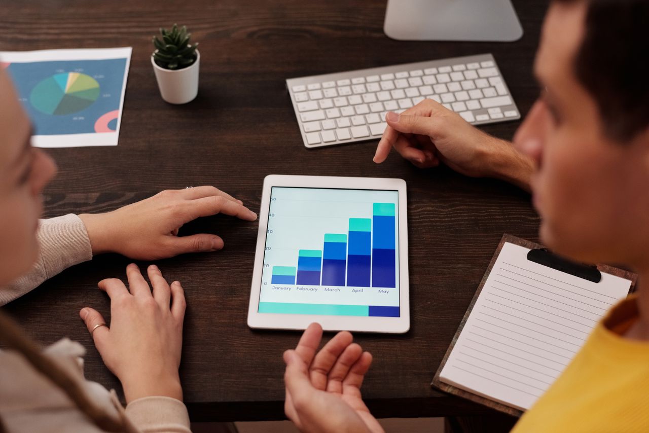 About Team members discussing digital graphs on a tablet in a modern office setting.